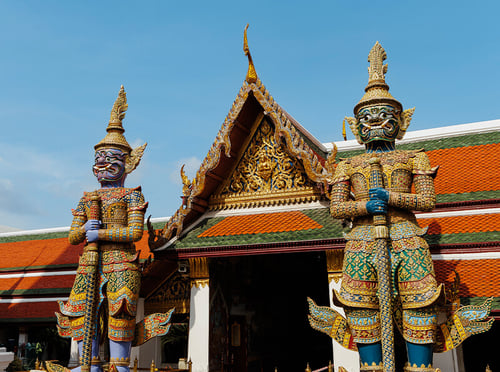 Gilded spires of the Grand Palace rising above the Chao Phraya River at dusk in Bangkok, Thailand