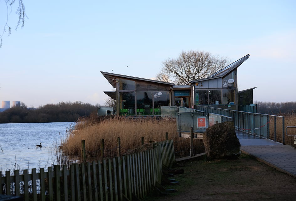 The Attenborough Nature Reserve visitor centre at dusk, situated on the waterside with reeds in the foreground