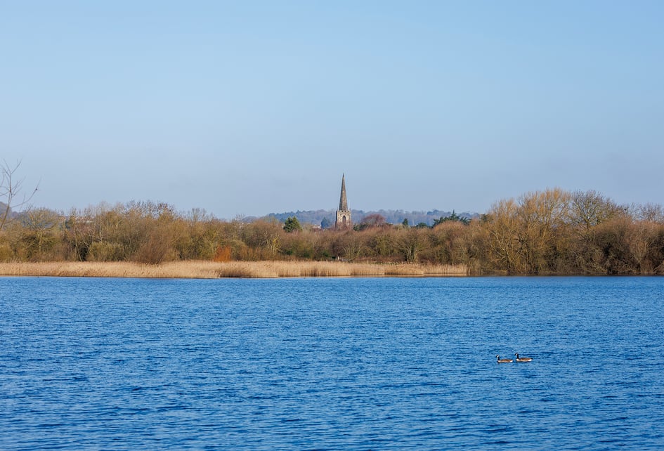 Wide view across the main lake at Attenborough Nature Reserve on a clear winter day, with a church spire visible on the horizon